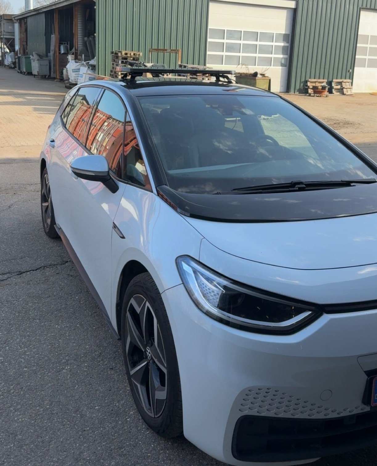 Hvid Volkswagen ID.3 med lysbro på taget ved en værkstedsbygning